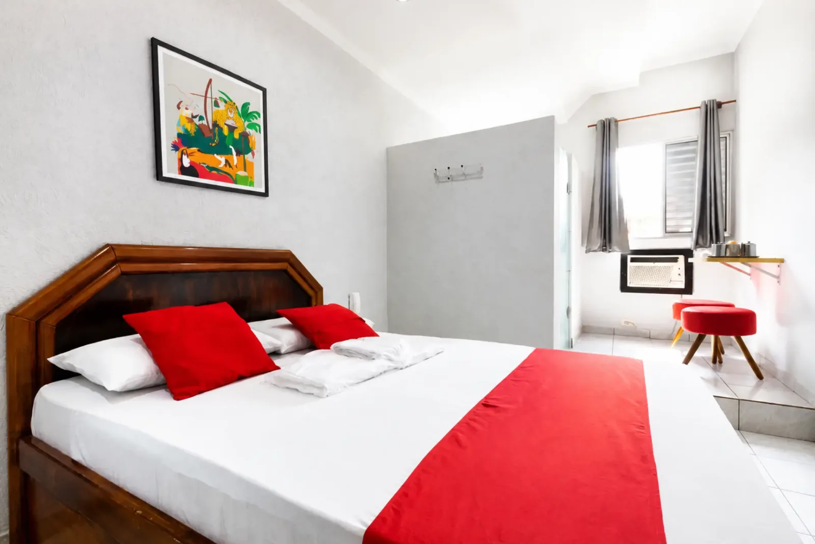 Suíte Standard com cama ampla, detalhes em vermelho e janela iluminada